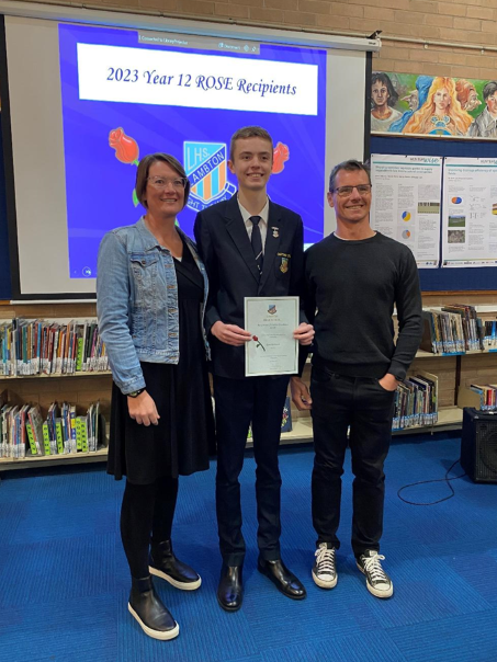 A male high school student and his parents smiling with an award.