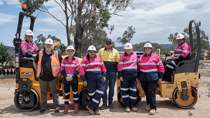 Group of people in PPE in front of two road rollers.