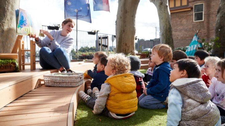 Female teacher giving demonstration outside while students sit on the ground