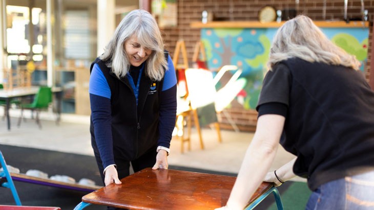 Two early childhood education and care educators set up outside play equipment.
