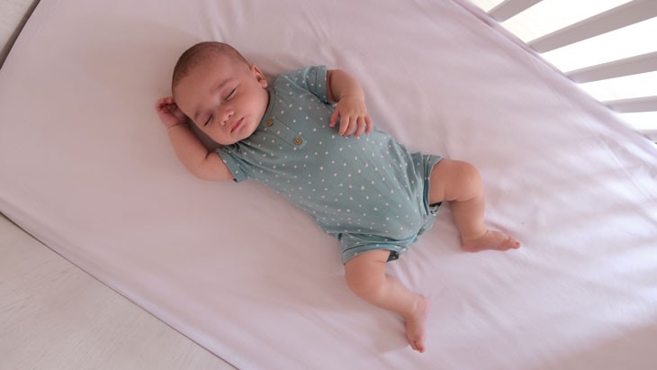 A close up of a baby laying down on its back sleeping in a crib.