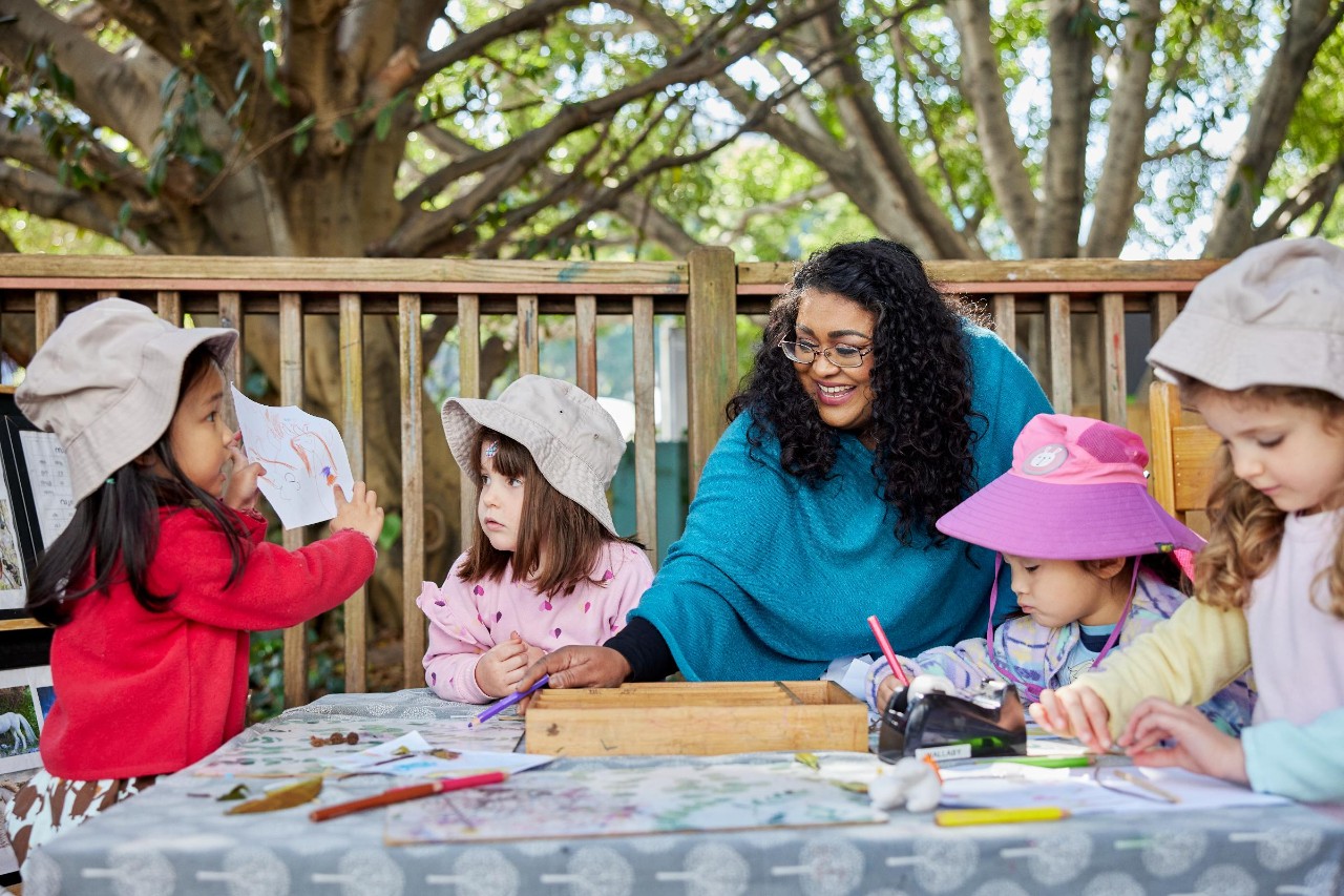 Female educator drawing with girls on a table outside