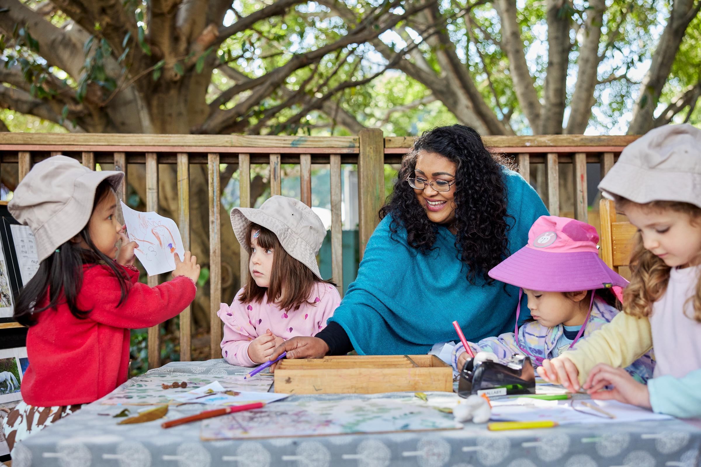 Female educator drawing with girls on a table outside
