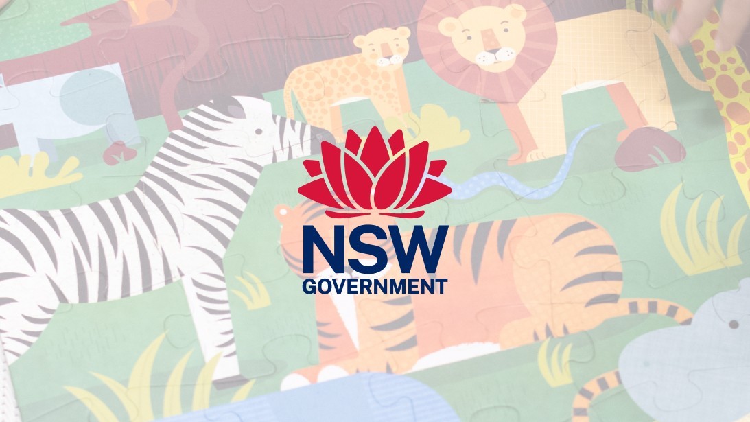 The NSW Government logo is against a blurred background photo of an animal puzzle