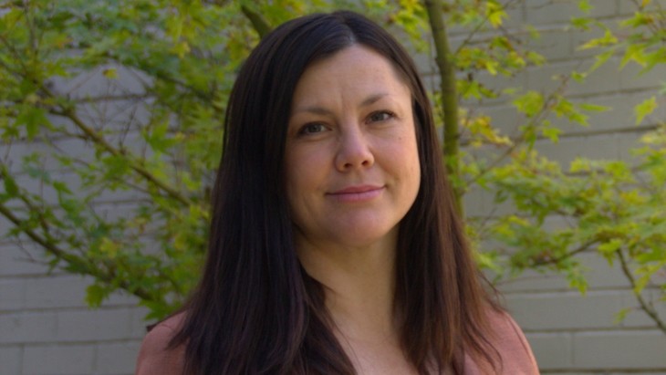A close up of a woman standing outside in front of a green tree.