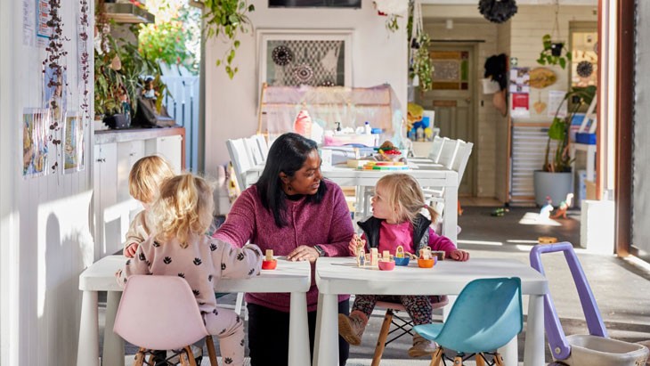 An educator sits with 3 children at a family day care residence.