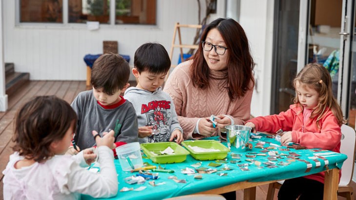 Students working on colourful table outside with teacher