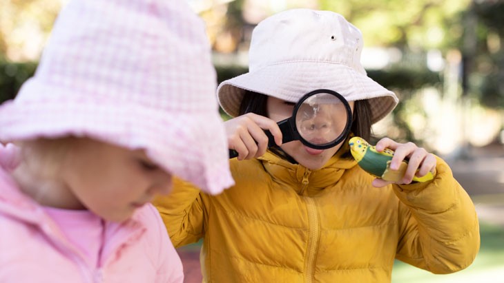 A child looks at a toy bird through a magnifying glass.