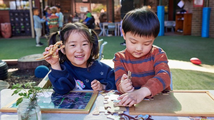 Two young children sitting outside completing a puzzle.