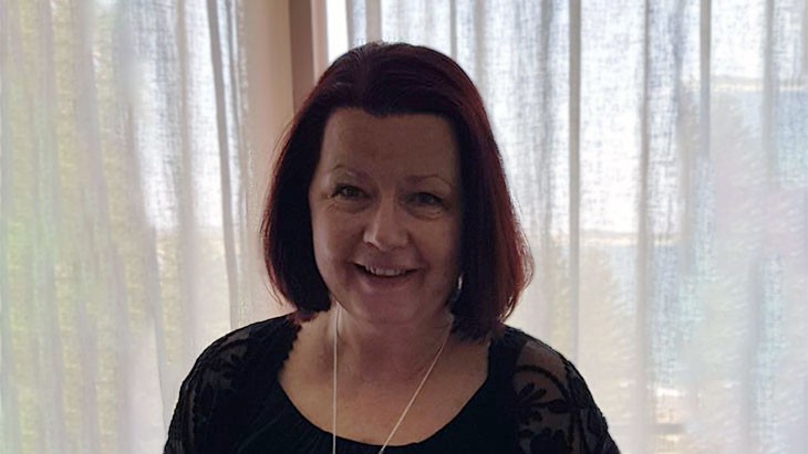 Photo from the shoulders up showing a smiling woman with shoulder-length reddish-brown hair.