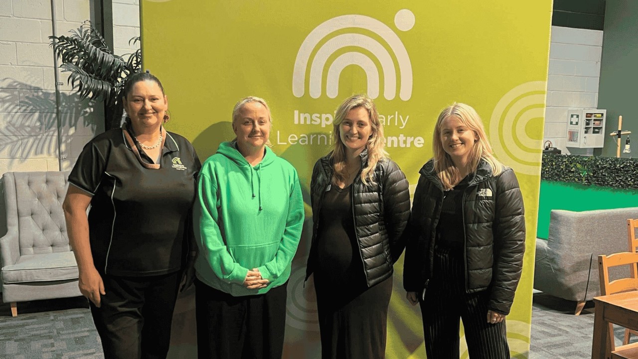 Four educators stand in a service in front of a green sign