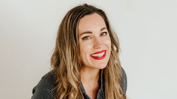 A smiling woman with bright red lipstick and long light brown hair.