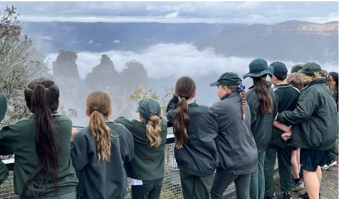 A group of primary school students dressed in green school uniform standing at a Blue Mountains lookout and looking at the Three Sisters