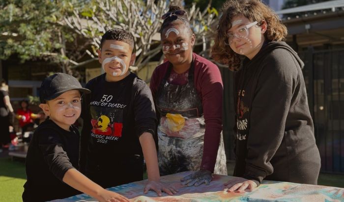 Three Aboriginal senior primary school students and an Aboriginal teacher doing hand paintings