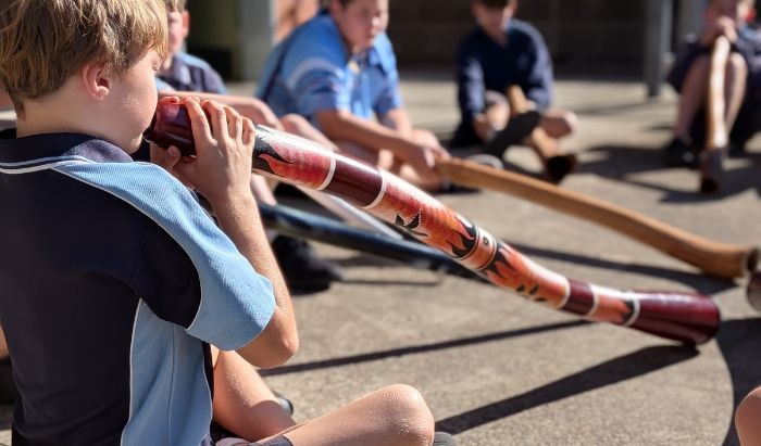 A primary school boy student dressed in blue school uniform playing the digeridoo
