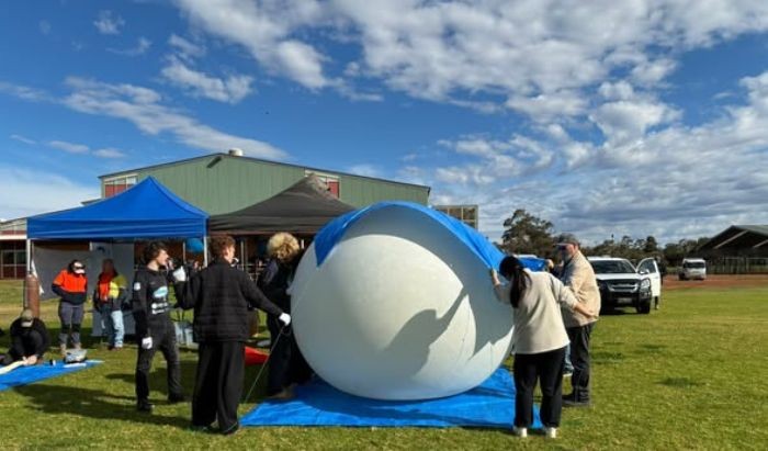 A group of people gathering around a weather balloon on the ground as they prepare to launch it