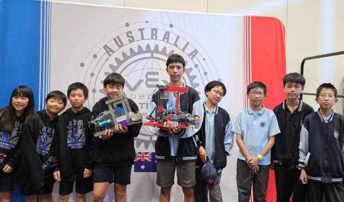 A group of senior primary school children two holding trophies in front of a red white and blue banner