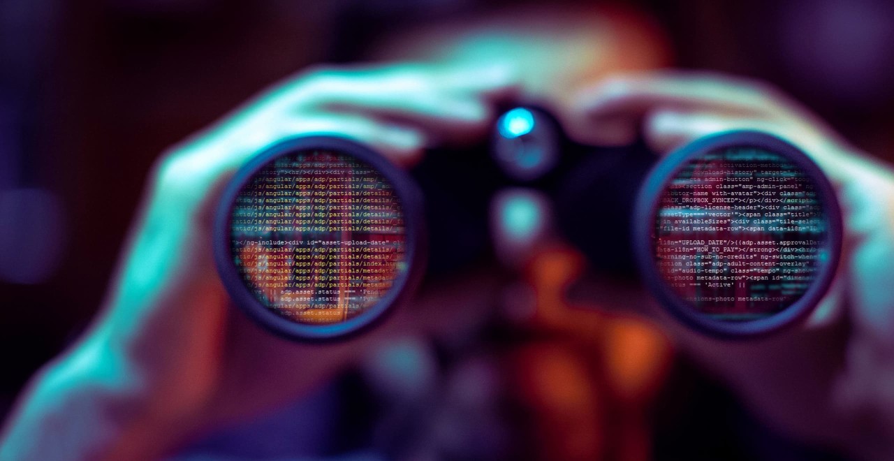 Person looking through binoculars. The lens of the binoculars is reflecting computer code. 
