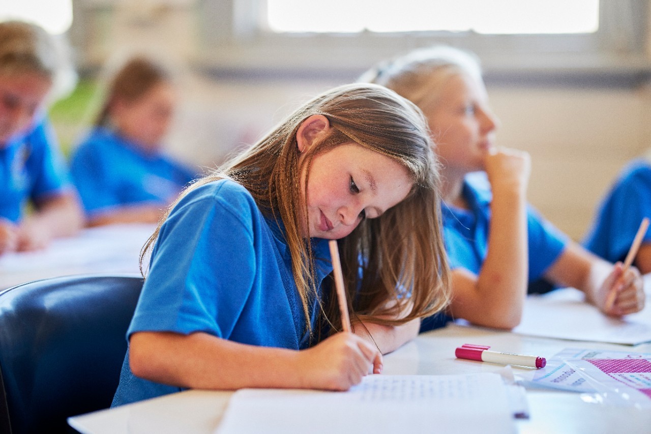Young female student sits at a desk and leans over her notebook while writing using a pencil