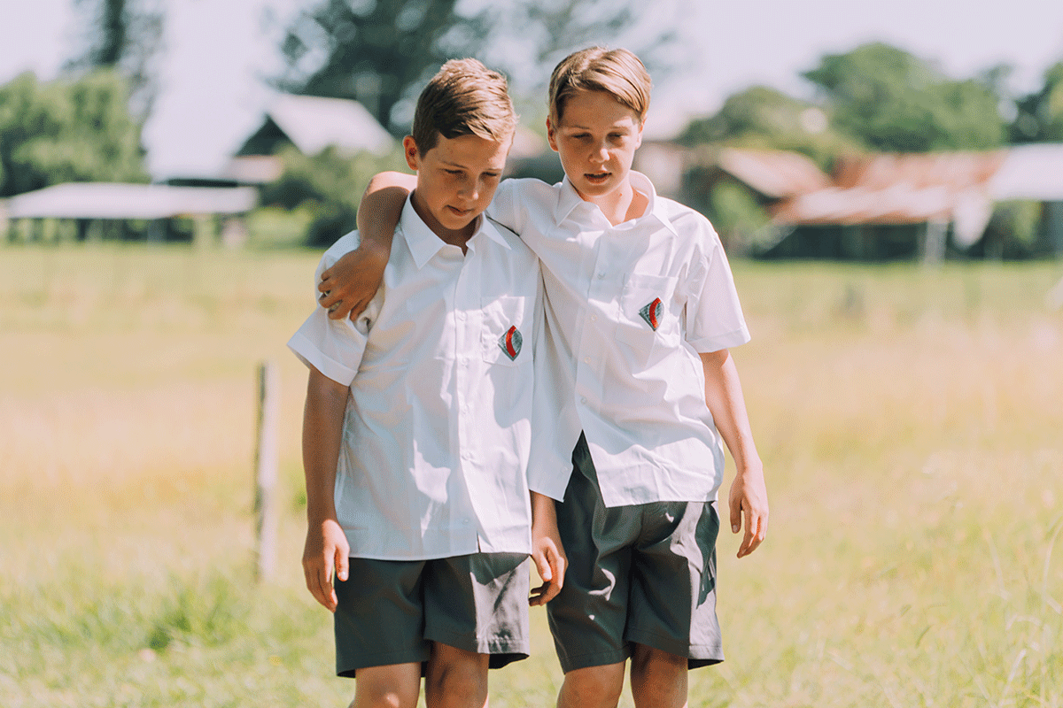 Two primary school aged boys in uniform on a paddock, in a supportive pose