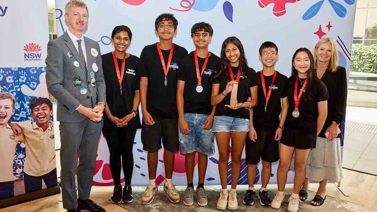 Adult male stands in a row next to female and 5 students.