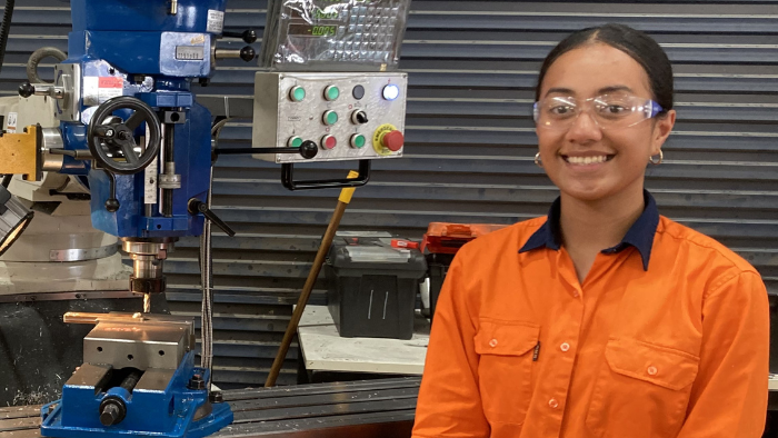 Harmony smiles at camera while posing with machinery