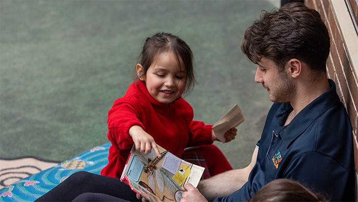 Young male child care worker reading a story to a girl.