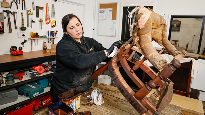 Female carpentry apprentice polishing restored wooden chair.