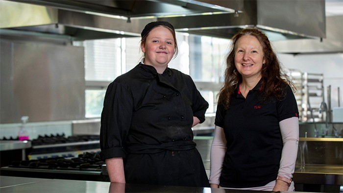 Female hospitality student with teacher in industrial kitchen.