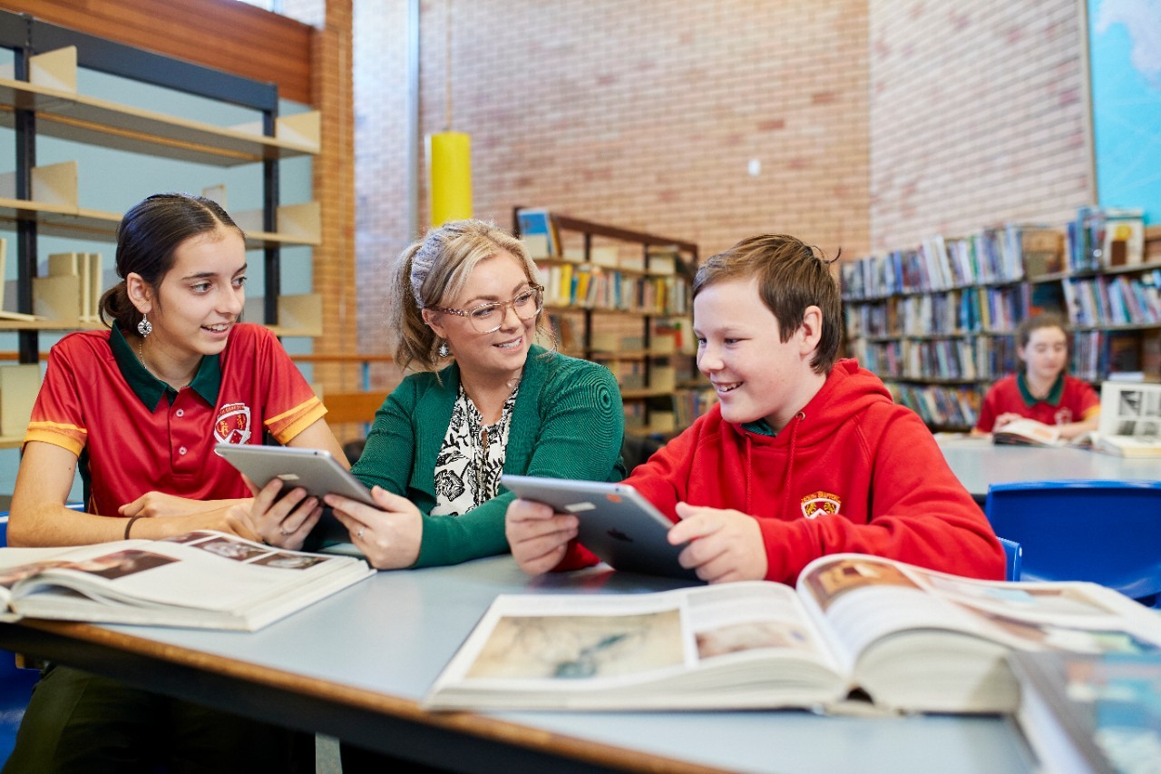 Female teacher sitting with two students on Ipads