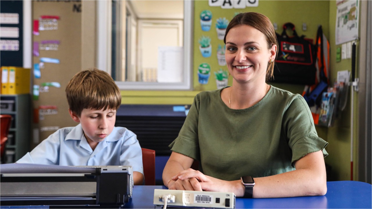 Female teacher sitting at desk with student on ipad