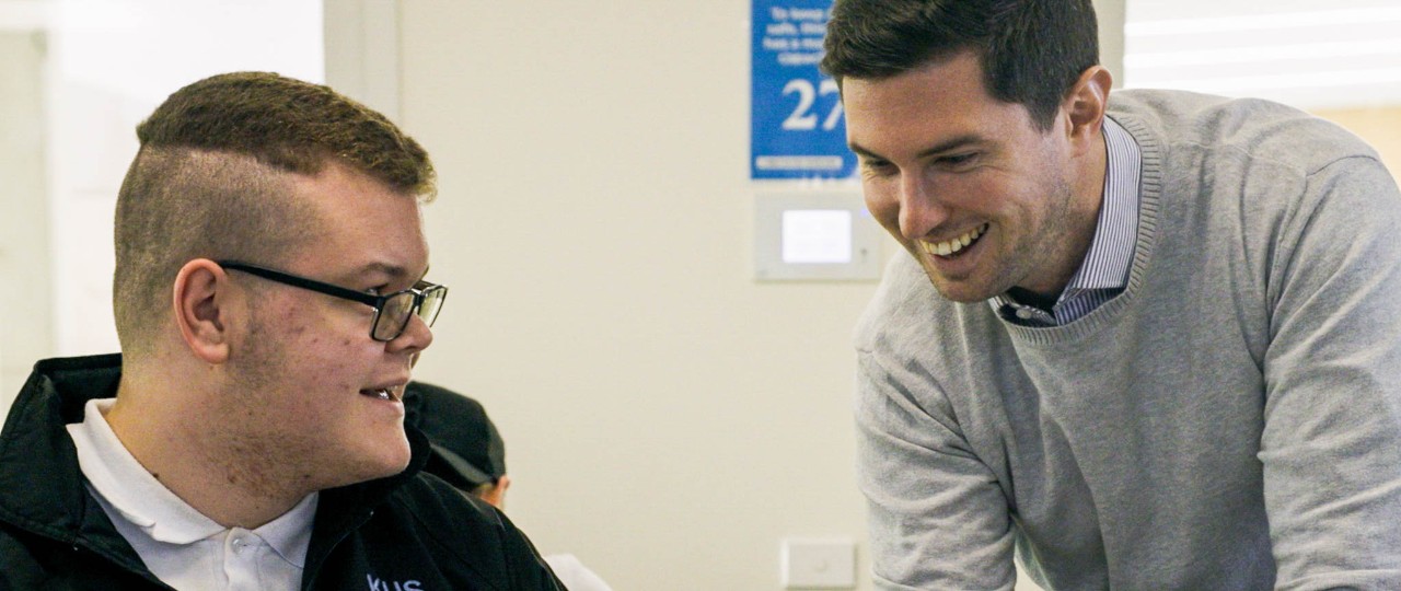 Male teacher helping student working on laptop