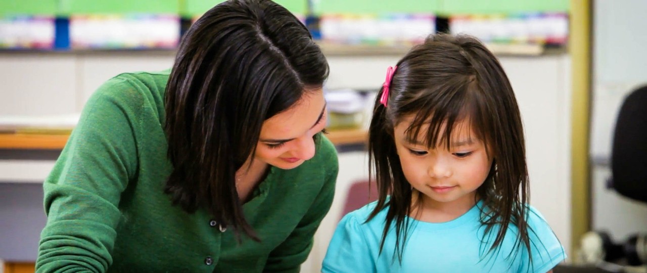 Female teacher reading a book with a female student