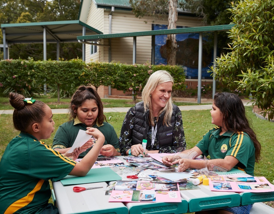 Primary students sitting outside with teacher doing craft