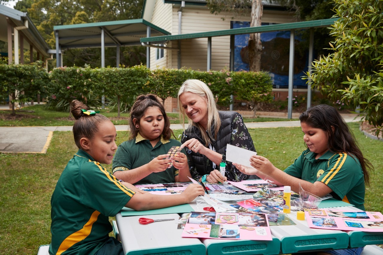 Primary school students outside doing craft with female teacher helping