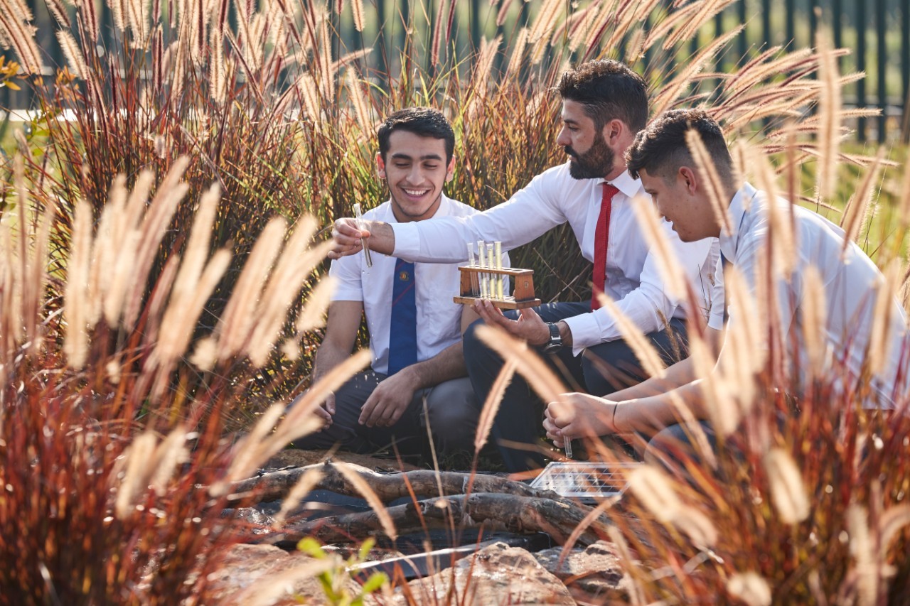 Male teacher holding test tube up, with two students watching