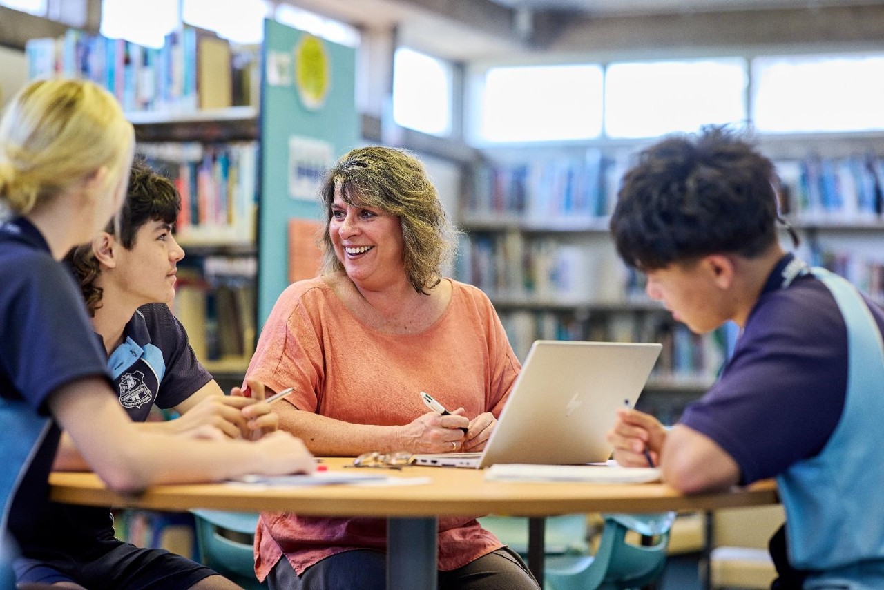Image of young people sitting at a desk talking to a teacher