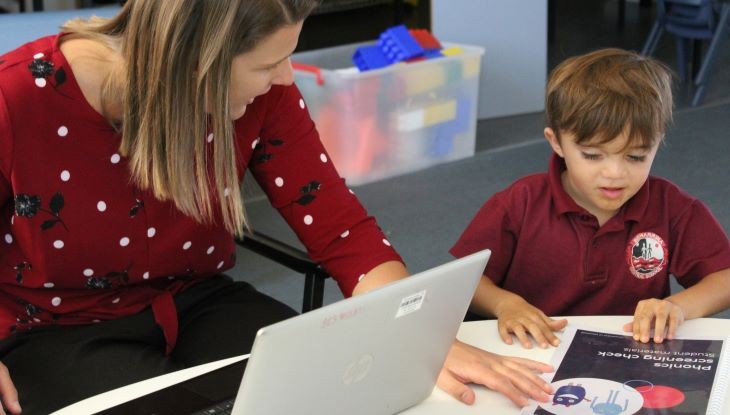 Teacher and primary student sitting at a table looking at assessment materials