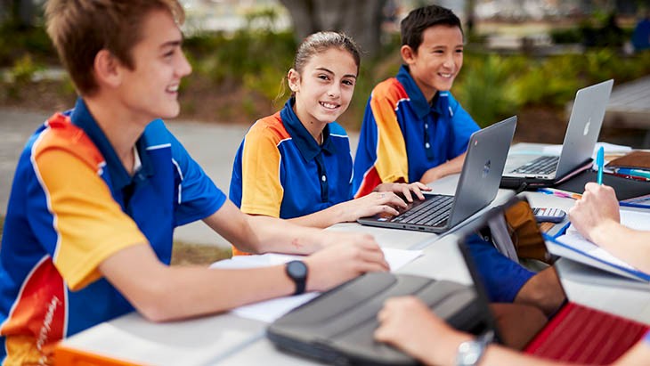 High school students sitting outside using computers