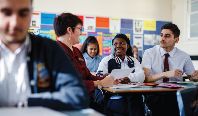 female eal/d teacher holding worksheet and speaking with two high school students in a classroom environment