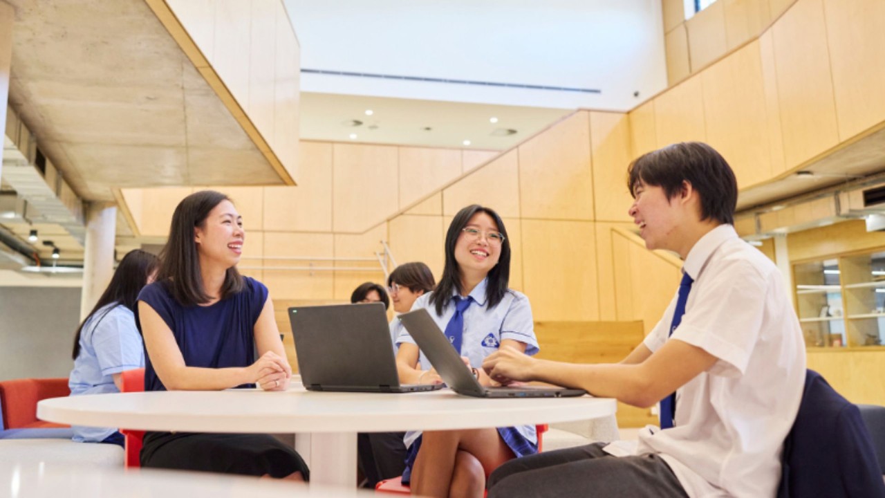 Teacher and students sitting at a desk talking and laughing.