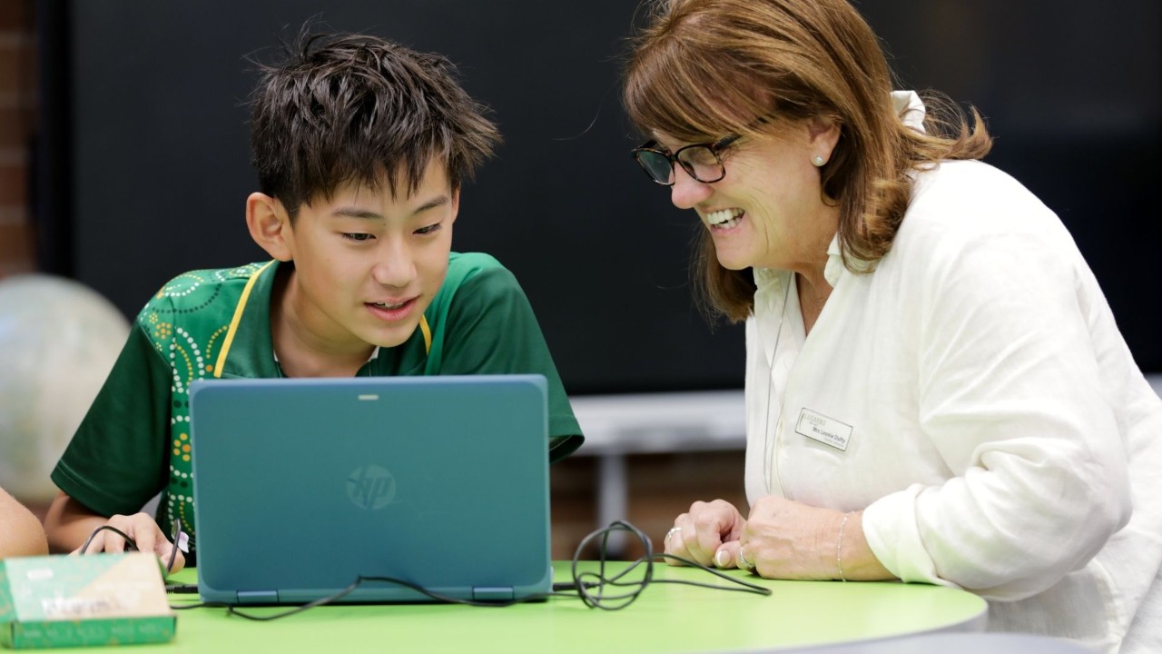 A teacher working with her student on a laptop