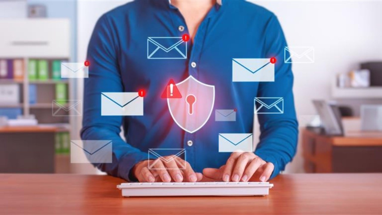 Person typing on a keyboard with transparent images of envelopes and a shield.