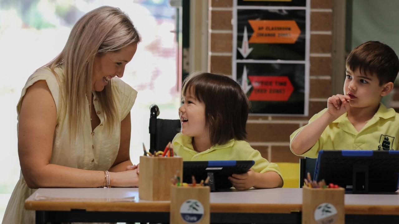 Teacher standing next to two students who are both using laptops.