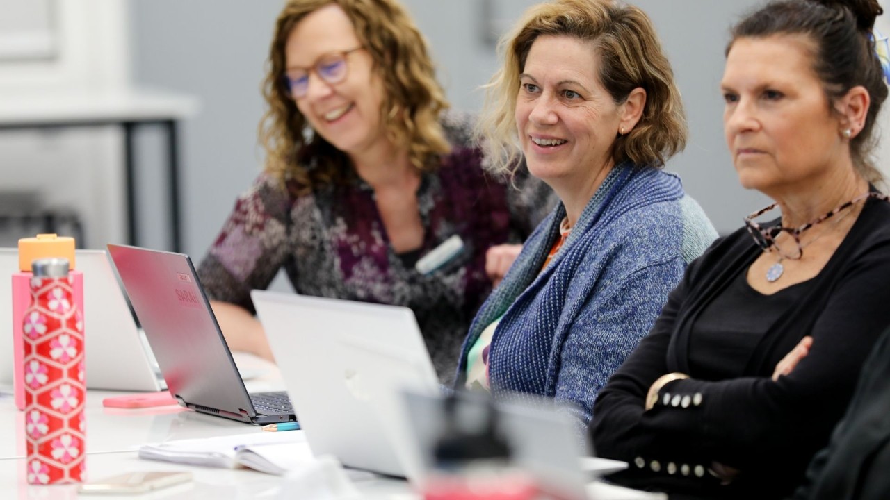Three ladies looking at their devices smiling.