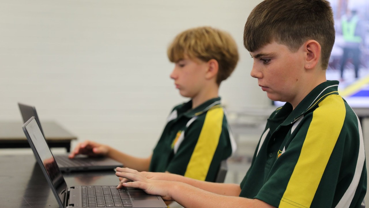 Two students sitting at a table working on a laptop.