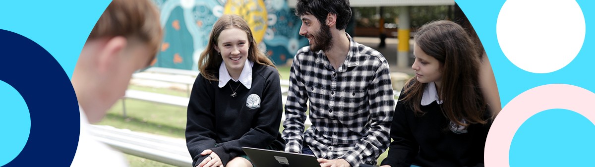 Teacher with students and MacBook on his lap.