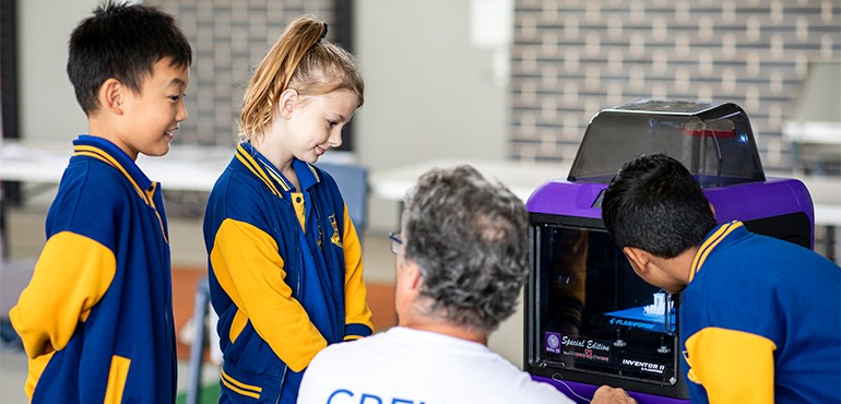Teacher working with students standing around a 3D printer.