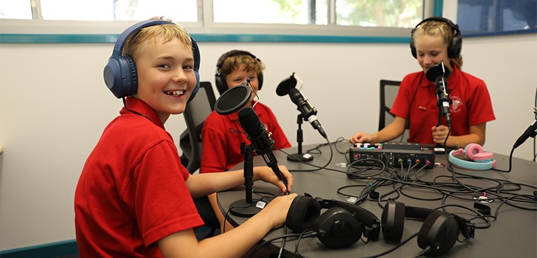 Students sitting at a table with headphones on using pod casting equipment.